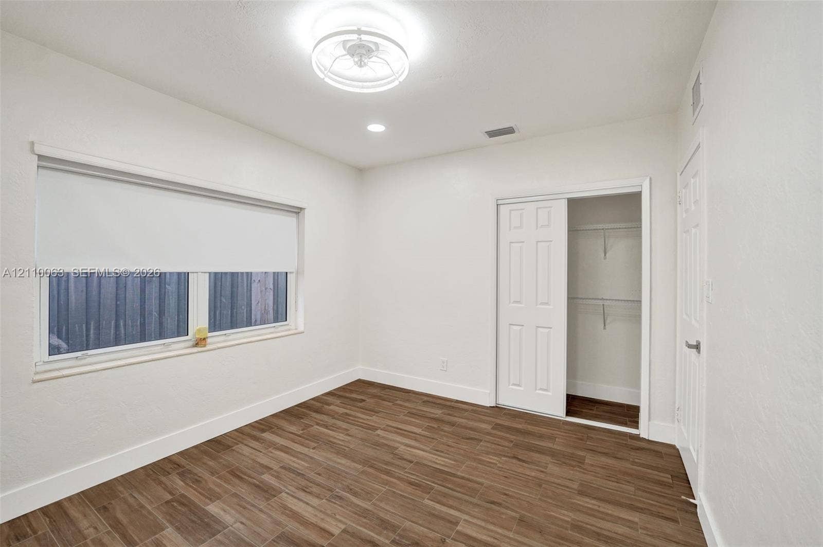 Room featuring wood-finish tile flooring, white walls, a multi-panel sliding closet door, and a circular flush-mount ceiling light fixture