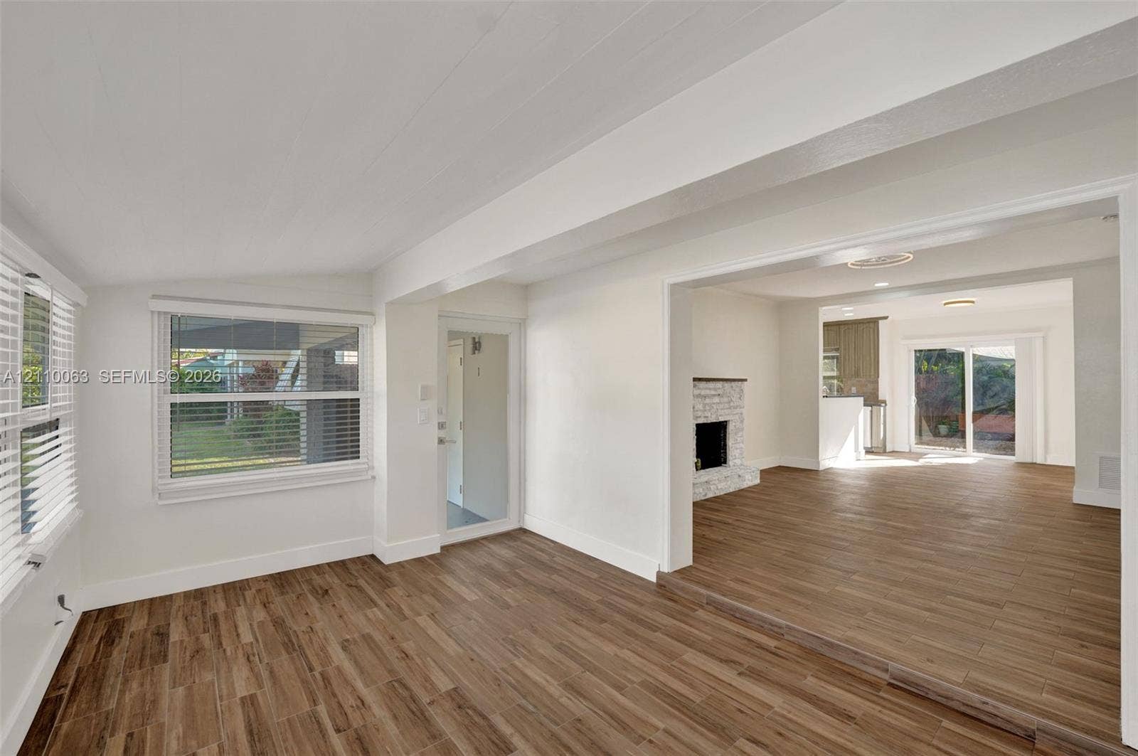 Interior space featuring wood-finish tile flooring, exposed structural beams, a brick fireplace, and sliding glass patio doors