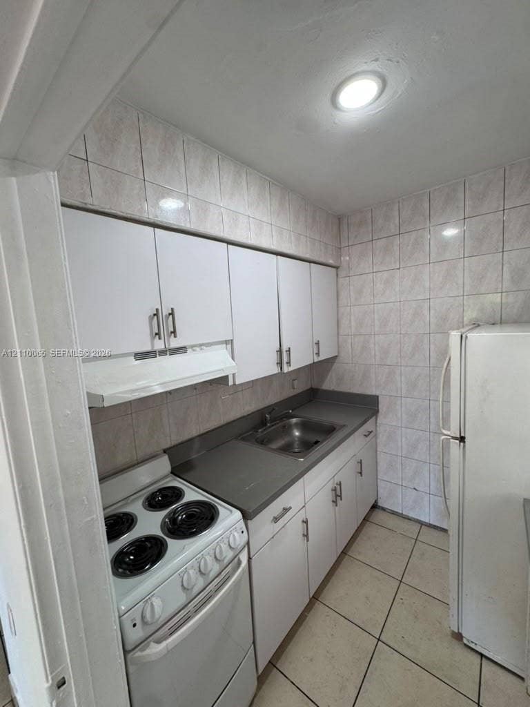 1701 NW 27th Avenue, #14, Miami, Miami, FL 33125 Kitchen featuring white cabinetry with metallic hardware, solid-surface countertops, a stainless steel basin sink, ceramic wall tiling, and ceramic floor tiling