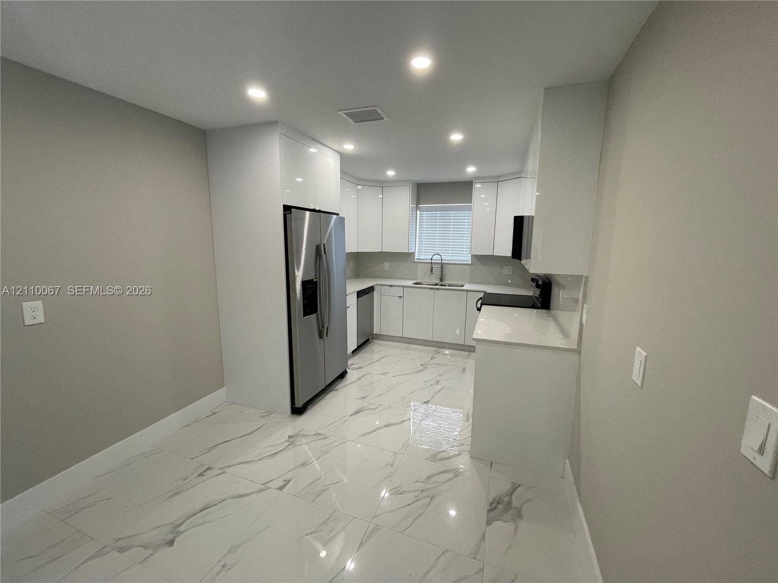 Large format, stone-finish tile flooring, recessed ceiling lighting, dual French doors providing exterior access, and a kitchen featuring built-in cabinetry