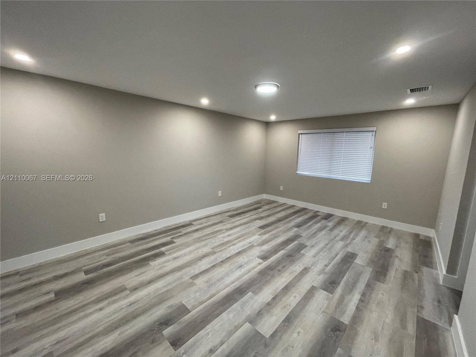 Neutral-toned walls featuring wood-finish flooring, a flush-mount ceiling light fixture, a six-panel door, and horizontal window blinds
