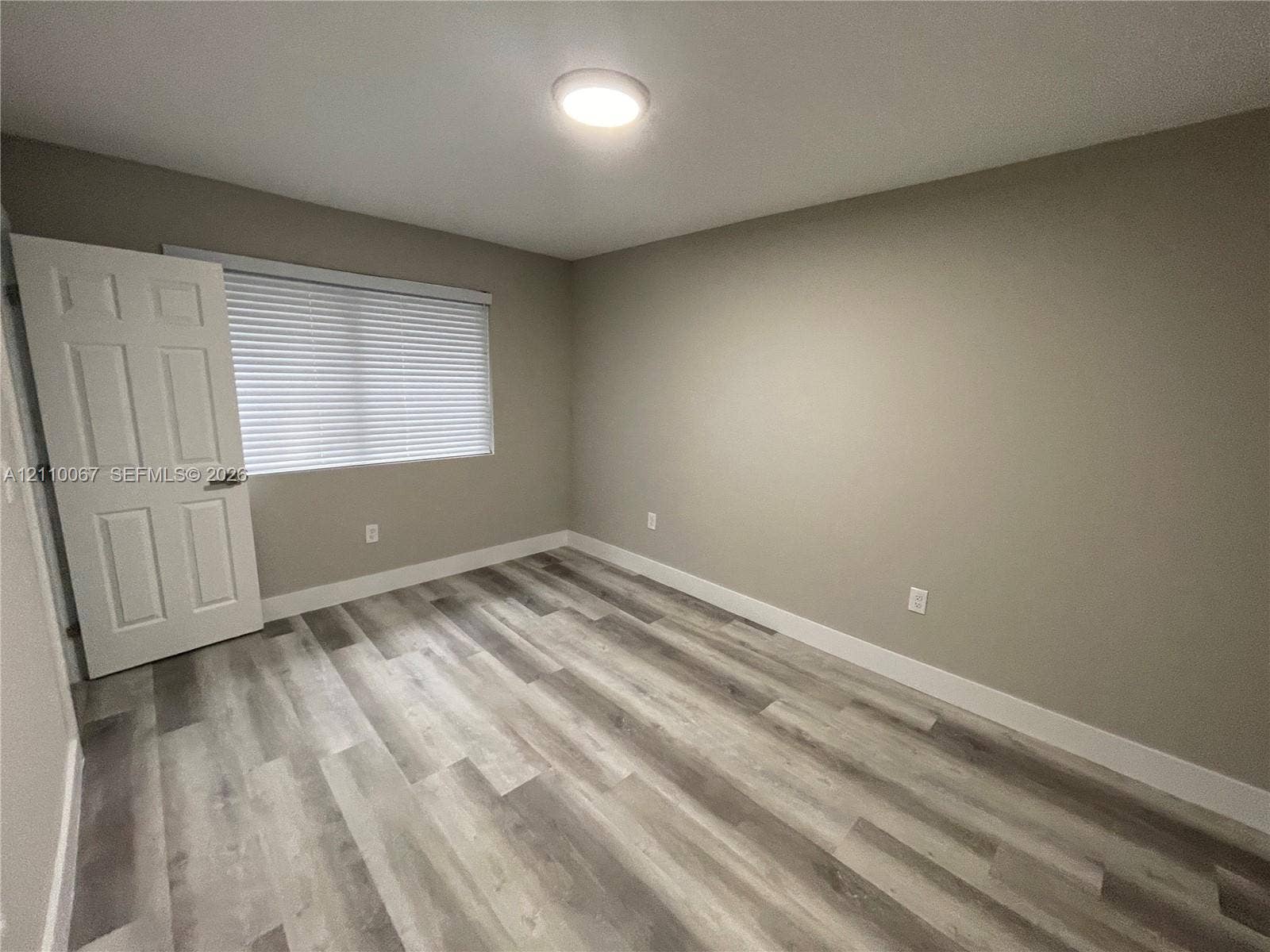 Bathroom featuring wood-finish flooring, a vanity with a solid surface countertop and undermount sink, a framed wall mirror, and a tub shower combination with large-format wall tile and a built-in recessed niche
