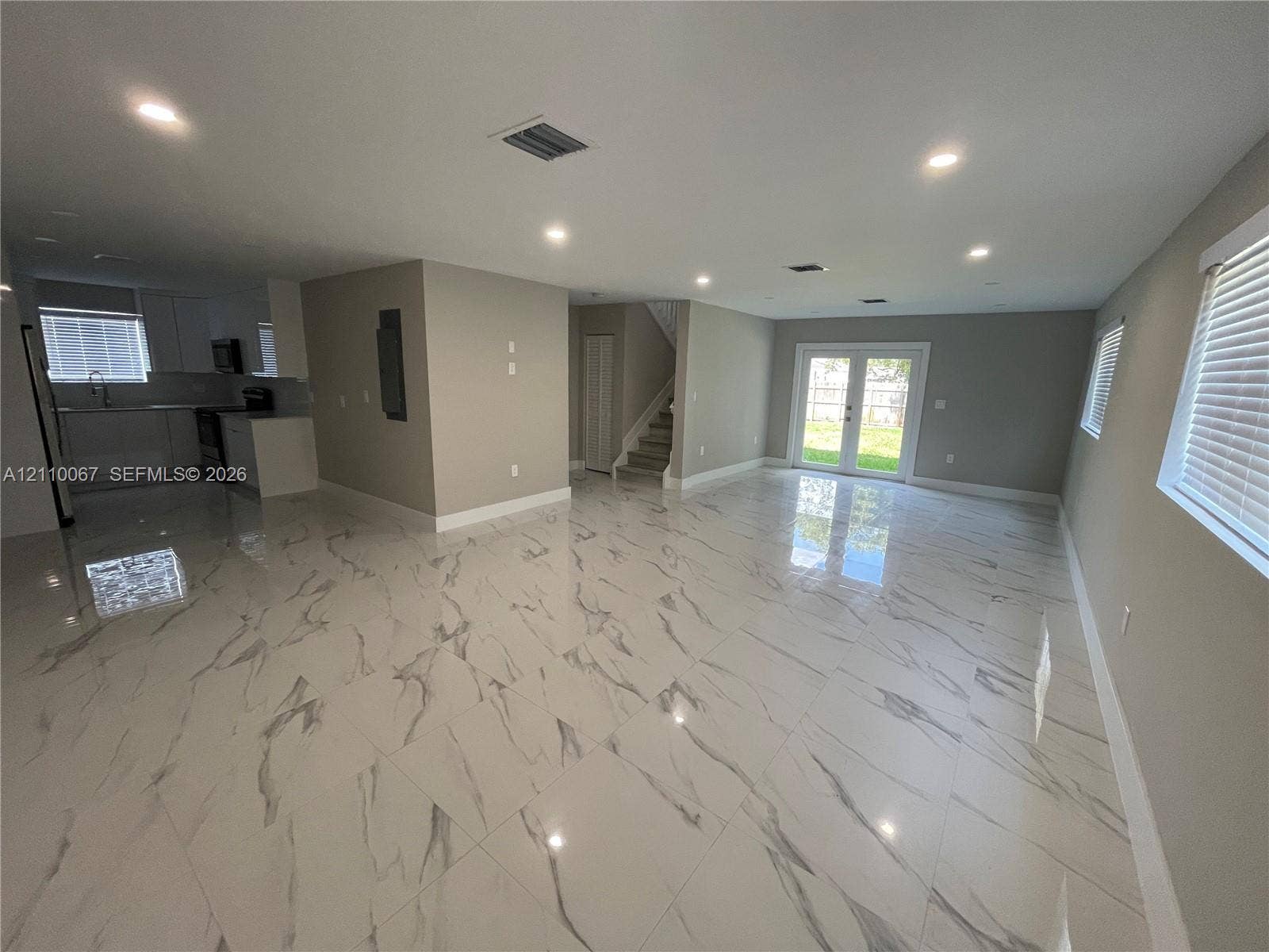 Two-story exterior featuring a white stucco facade, arched covered entryway, hip roofline, concrete driveway, and installed privacy fencing