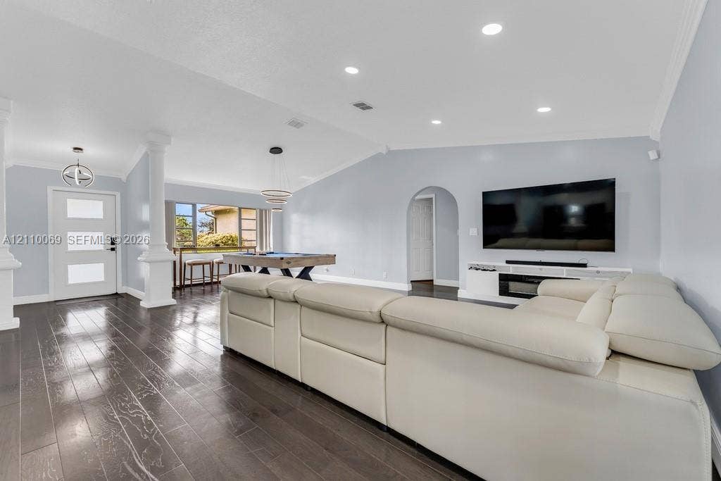 4325 NW 95th Terrace, Sunrise, FL 33351 Open-concept interior featuring vaulted ceilings, dark wood-finish flooring, recessed lighting, architectural columns, and a built-in media console with an integrated fireplace