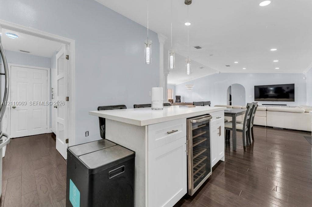 4325 NW 95th Terrace, Sunrise, FL 33351 Kitchen island featuring a solid-surface countertop, white shaker-style cabinetry, an integrated stainless steel wine refrigerator, and triple pendant lighting