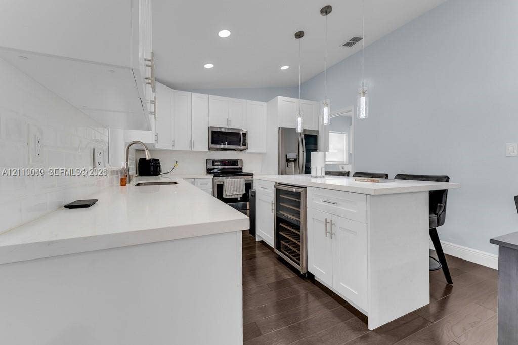 4325 NW 95th Terrace, Sunrise, FL 33351 Kitchen featuring white cabinetry, quartz countertops, a central island with a built-in wine cooler, wood-finish flooring, and pendant lighting