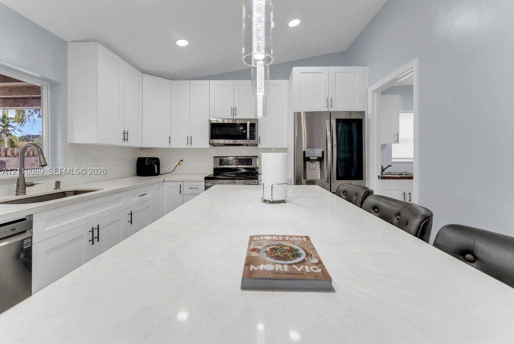 4325 NW 95th Terrace, Sunrise, FL 33351 Kitchen featuring white shaker-style cabinetry, a quartz-surfaced center island, stainless steel appliances, recessed lighting, and a dual-basin undermount sink with a high-arch faucet