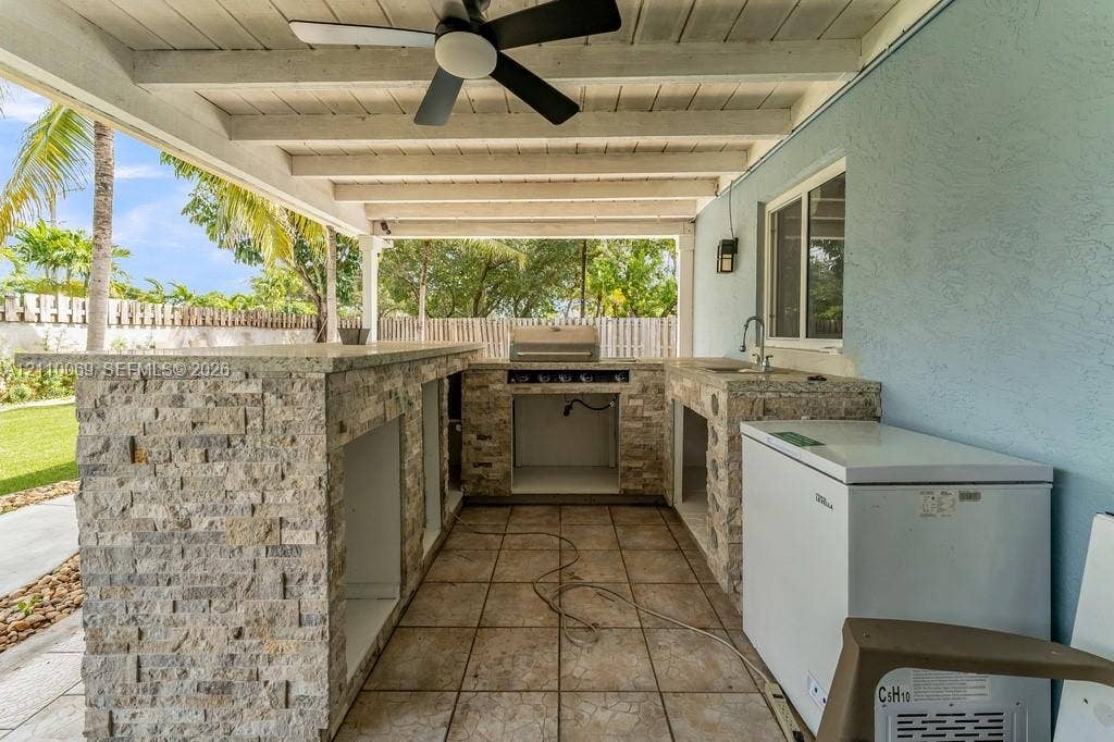 4325 NW 95th Terrace, Sunrise, FL 33351 Covered outdoor kitchen featuring stone veneer cabinetry, solid surface countertop, built-in grill, integrated sink, and overhead ceiling fan