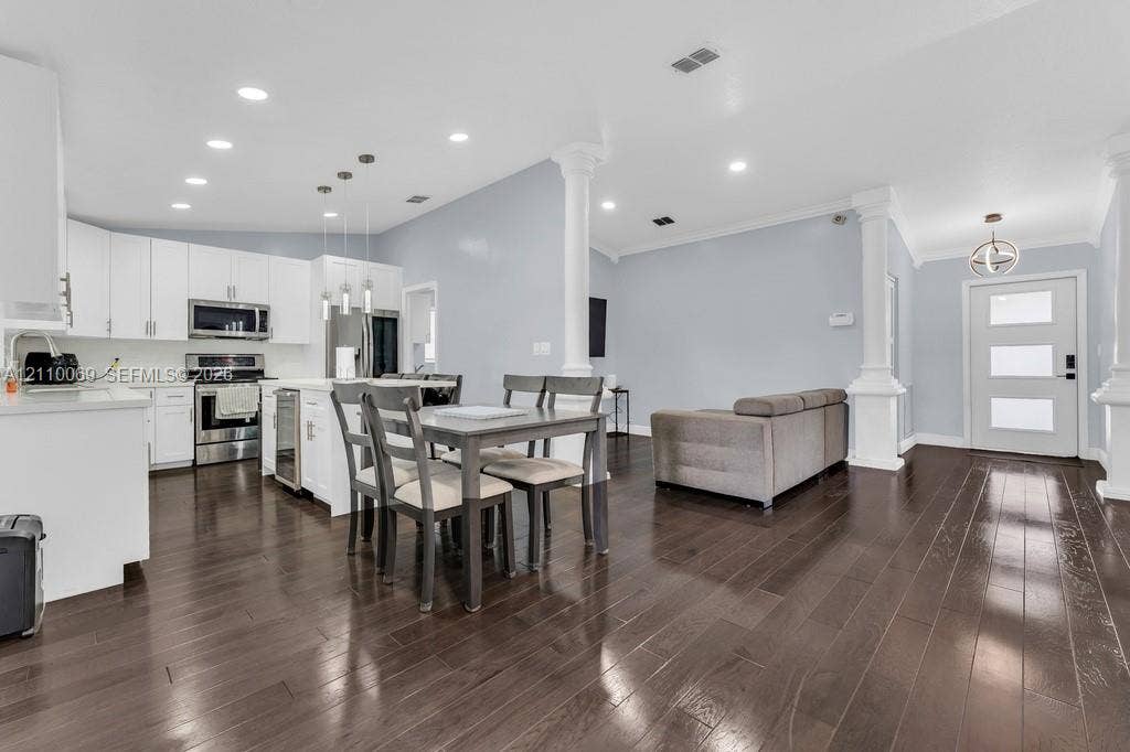 4325 NW 95th Terrace, Sunrise, FL 33351 Open-concept kitchen and living area featuring dark wood-finish flooring, white cabinetry, stainless steel appliances, decorative structural columns, and recessed lighting