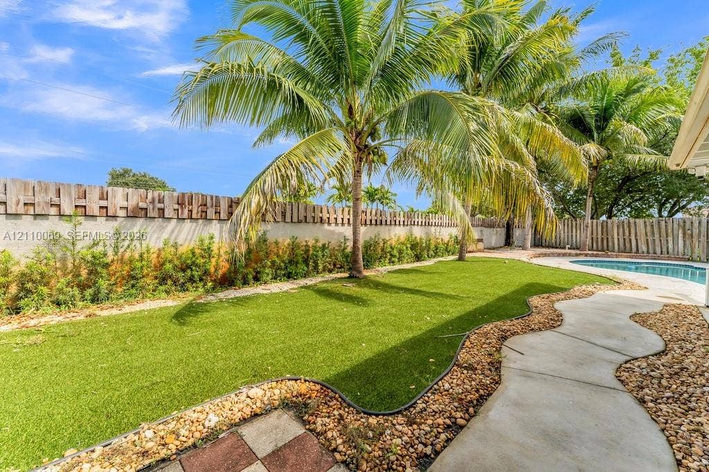 4325 NW 95th Terrace, Sunrise, FL 33351 Fenced backyard featuring synthetic turf, palm trees, stone-pebble landscaping, concrete walkway, and a swimming pool