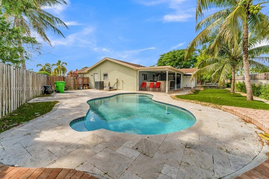 4325 NW 95th Terrace, Sunrise, FL 33351 Backyard featuring a free-form pool, stone-paver decking, covered patio with a built-in outdoor bar, and a fenced perimeter