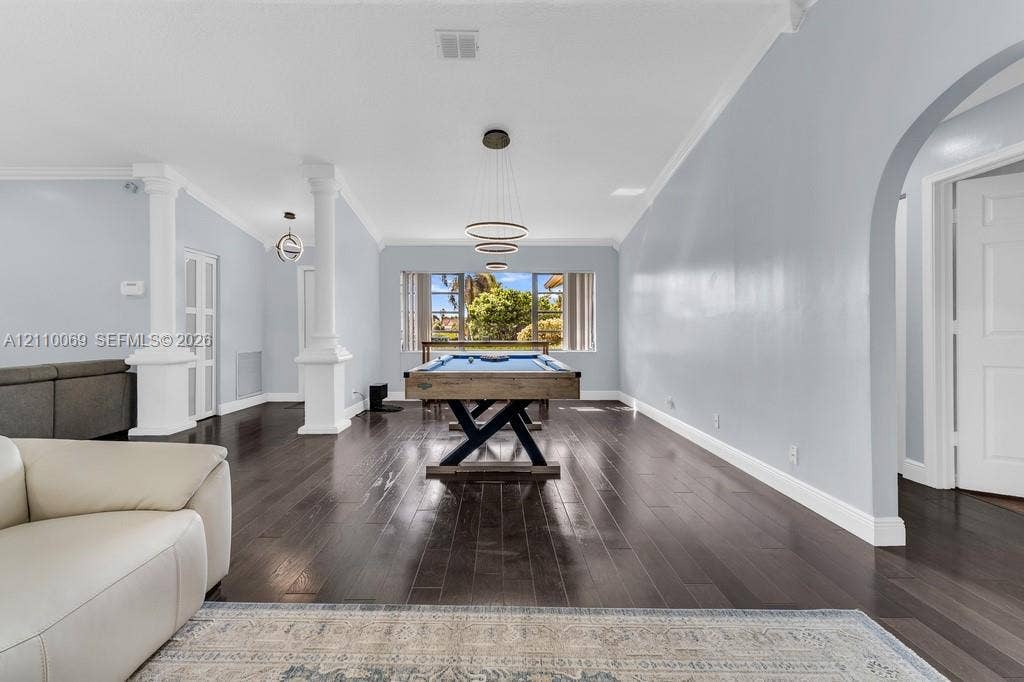 4325 NW 95th Terrace, Sunrise, FL 33351 Open-concept interior featuring wood-finish flooring, architectural columns, a multi-tiered circular pendant light, and an arched doorway