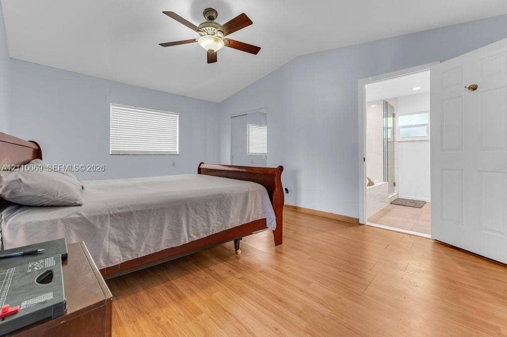 4325 NW 95th Terrace, Sunrise, FL 33351 Bedroom featuring wood-finish flooring, vaulted ceilings, ceiling fan with integrated lighting, window blinds, and mirrored closet doors