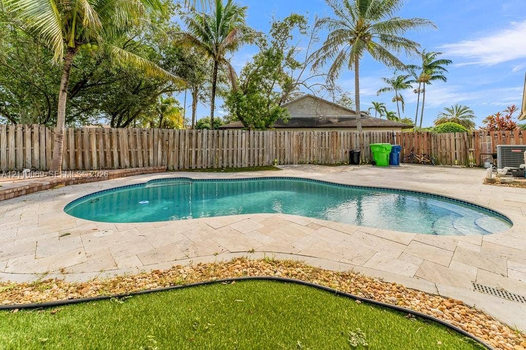 4325 NW 95th Terrace, Sunrise, FL 33351 Freeform swimming pool with stone-tiled patio, stone curbing, wood-style privacy fencing, and established palm trees