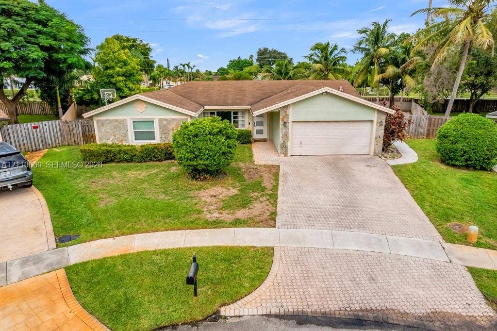 4325 NW 95th Terrace, Sunrise, FL 33351 Single-story exterior featuring stone veneer accents, a multi-gabled roofline, a paved driveway, and an attached two-car garage