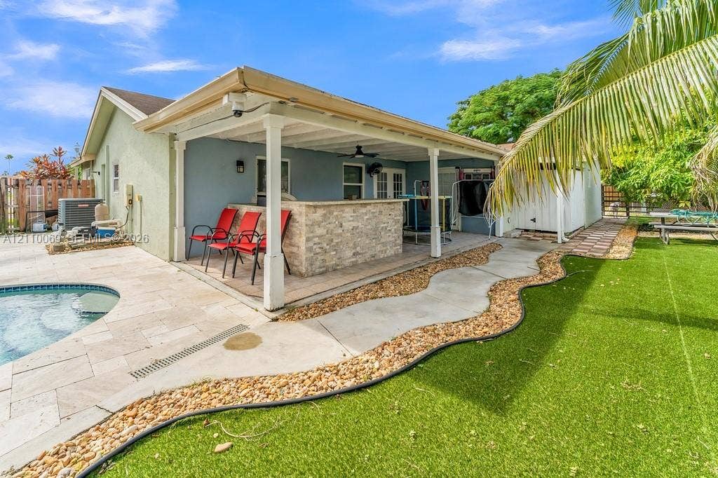 4325 NW 95th Terrace, Sunrise, FL 33351 Covered outdoor patio featuring a stone-faced built-in bar, tile pool deck, swimming pool, and artificial turf lawn