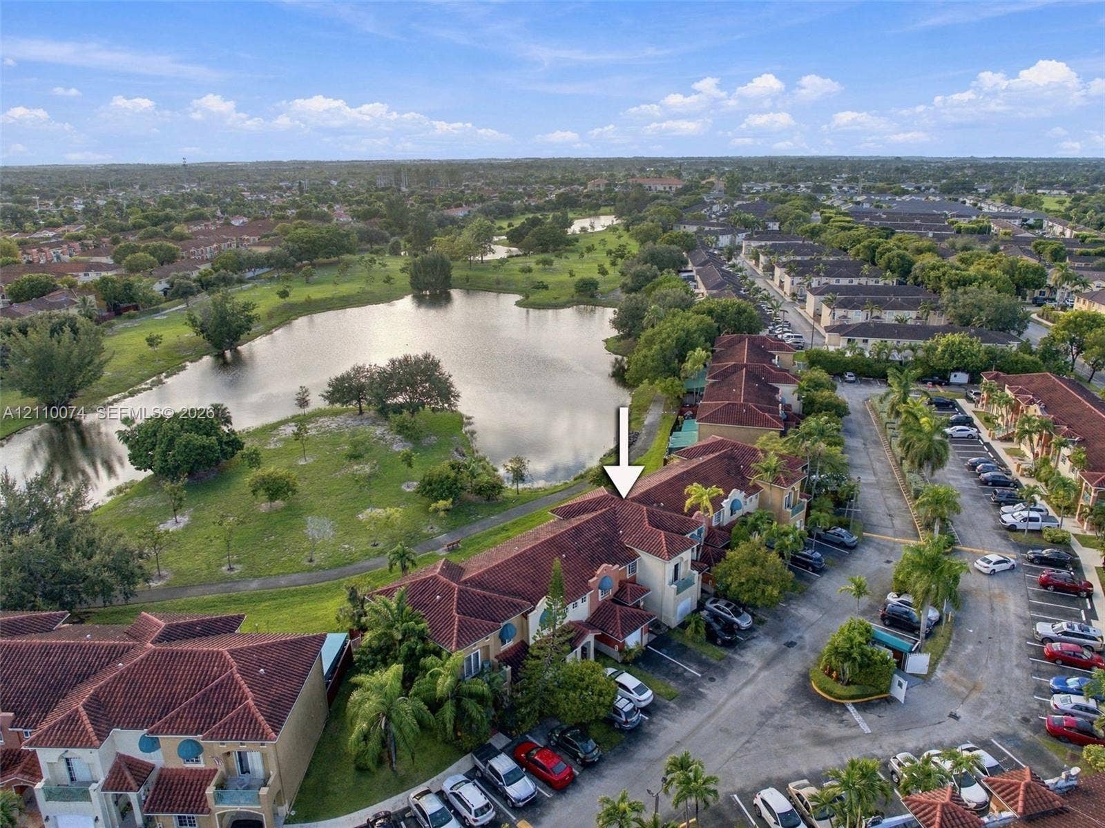 17370 NW 69th Court, #304, Hialeah, FL 33015 Aerial view featuring a multi-story residence with a multi-gabled tile roof, concrete exterior, balcony, and proximity to a community lake and green space