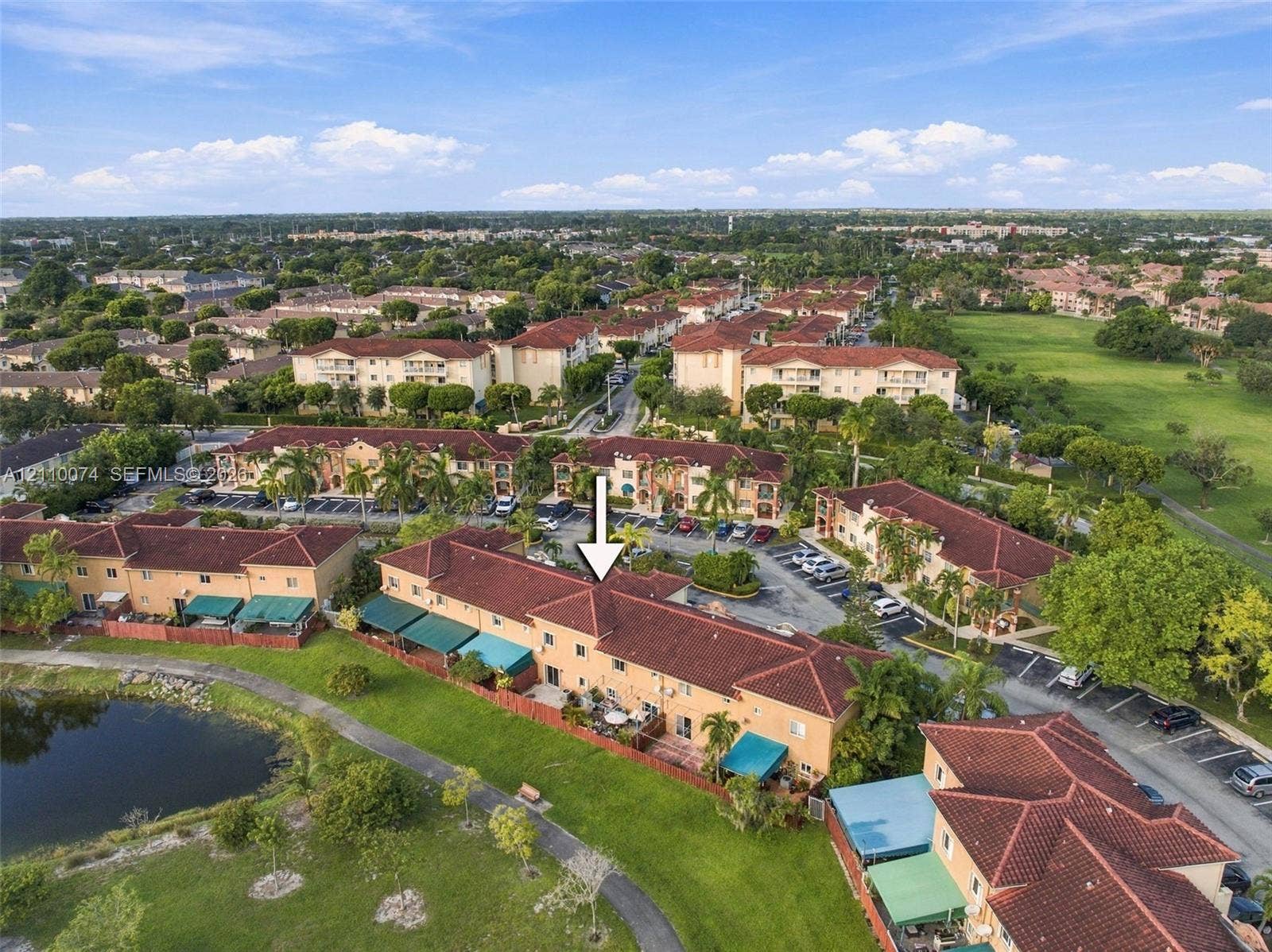 17370 NW 69th Court, #304, Hialeah, FL 33015 Aerial perspective of a multi-unit residential complex featuring terracotta-style roofing, stucco exterior finish, paved surface parking, and a waterfront location with mature landscaping