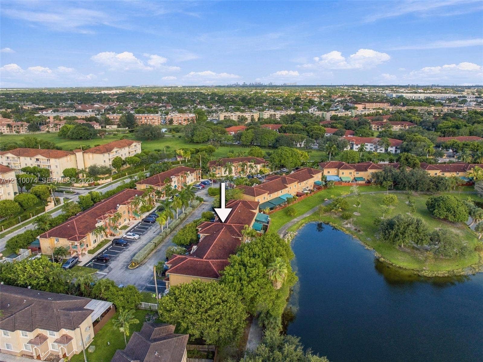 17370 NW 69th Court, #304, Hialeah, FL 33015 Aerial perspective of a multi-unit residential structure featuring a terracotta-style tiled roof, expansive water frontage, mature perimeter landscaping, and dedicated asphalt parking