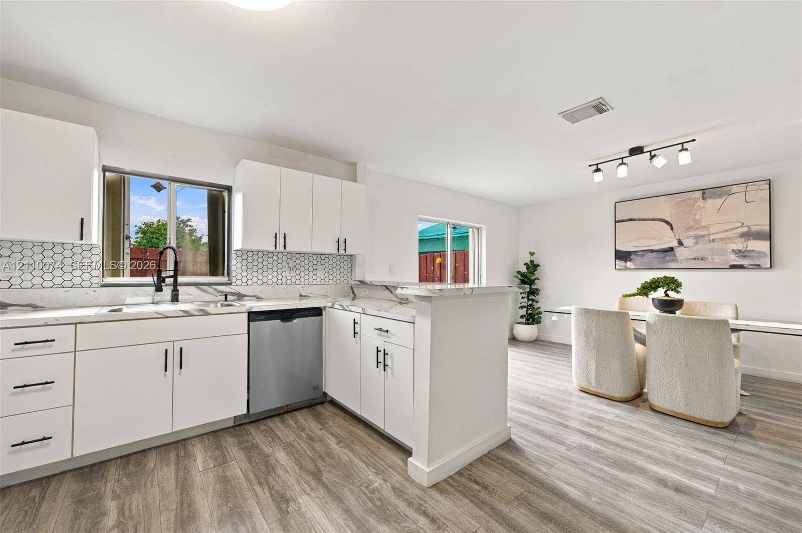 17370 NW 69th Court, #304, Hialeah, FL 33015 Kitchen featuring white cabinetry with matte black hardware, light-toned stone-finish countertops, geometric tile backsplash, stainless steel dishwasher, and wood-finish flooring