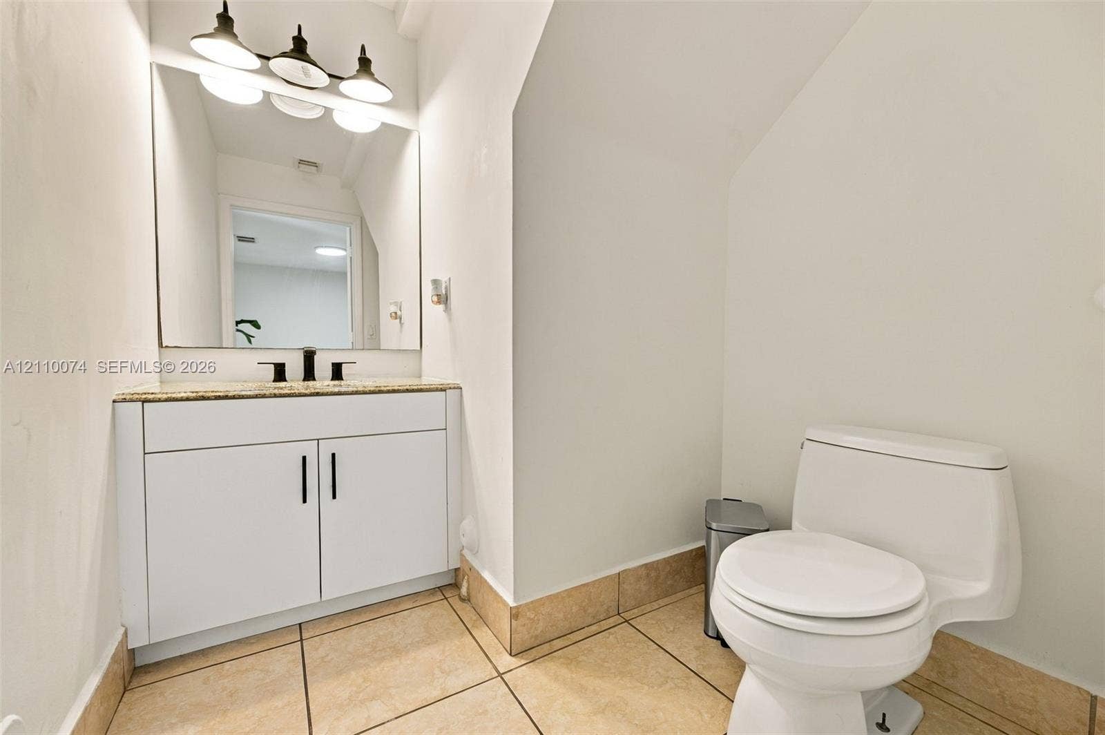 17370 NW 69th Court, #304, Hialeah, FL 33015 White vanity featuring stone-finish countertop, undermount sink with dark metal faucet, expansive wall mirror, three-light fixture, and ceramic tile flooring