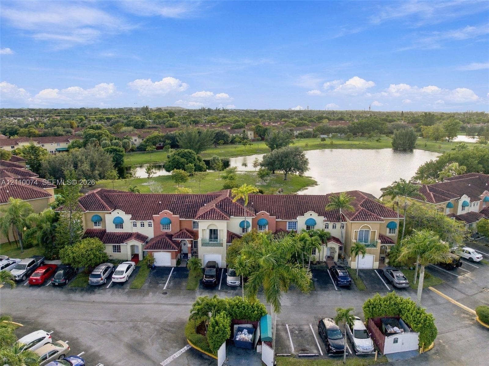 17370 NW 69th Court, #304, Hialeah, FL 33015 Multi-level townhome exterior featuring terracotta-style roof tiles, stucco facade, decorative blue window awnings, integrated garage bays, and mature palm landscaping