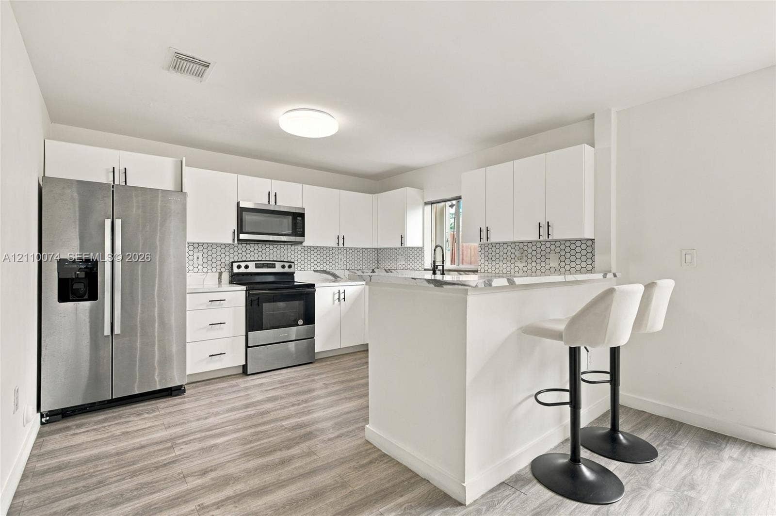 17370 NW 69th Court, #304, Hialeah, FL 33015 Kitchen featuring white cabinetry, stainless steel appliances, breakfast bar, stone-finish countertops, and wood-finish flooring