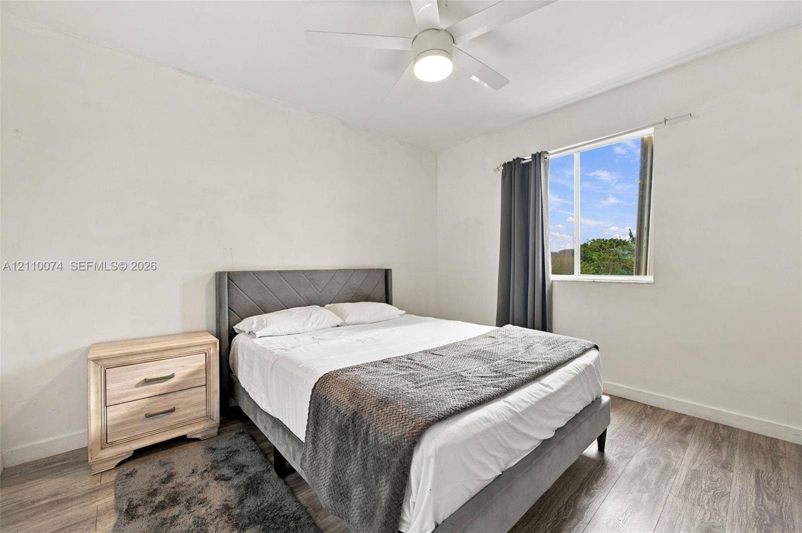 17370 NW 69th Court, #304, Hialeah, FL 33015 Neutral-toned room featuring wood-finish flooring, a white ceiling fan with integrated lighting, and a single-pane window