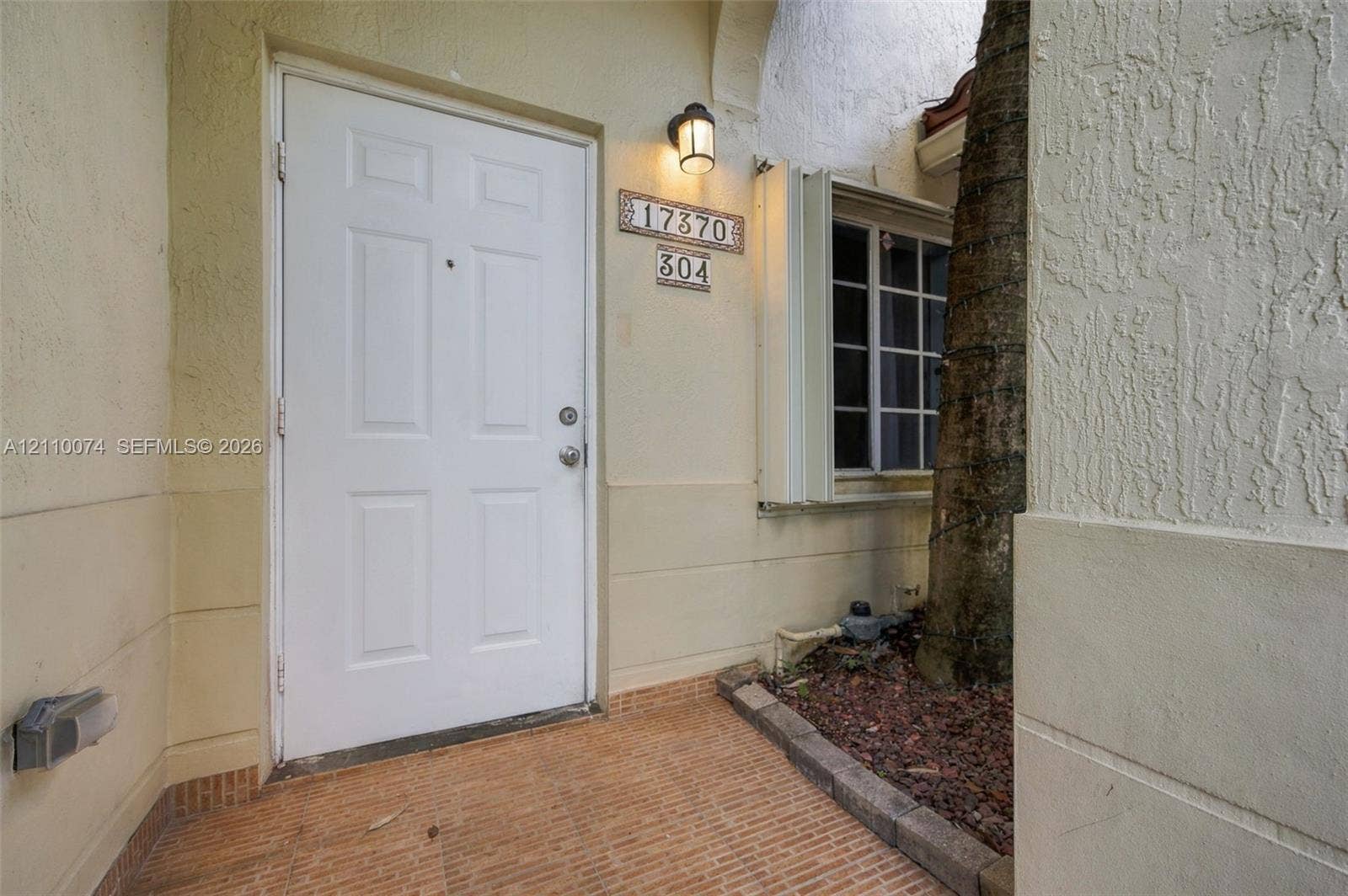 17370 NW 69th Court, #304, Hialeah, FL 33015 Stucco exterior entryway featuring a six-panel door, masonry tile flooring, recessed wall-mounted lighting, and a multi-pane window
