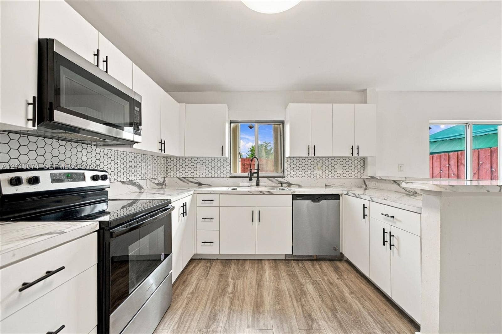 17370 NW 69th Court, #304, Hialeah, FL 33015 Kitchen featuring white cabinetry with matte black hardware, stone-patterned countertops, hexagonal tile backsplash, stainless steel appliances, and wood-finish flooring