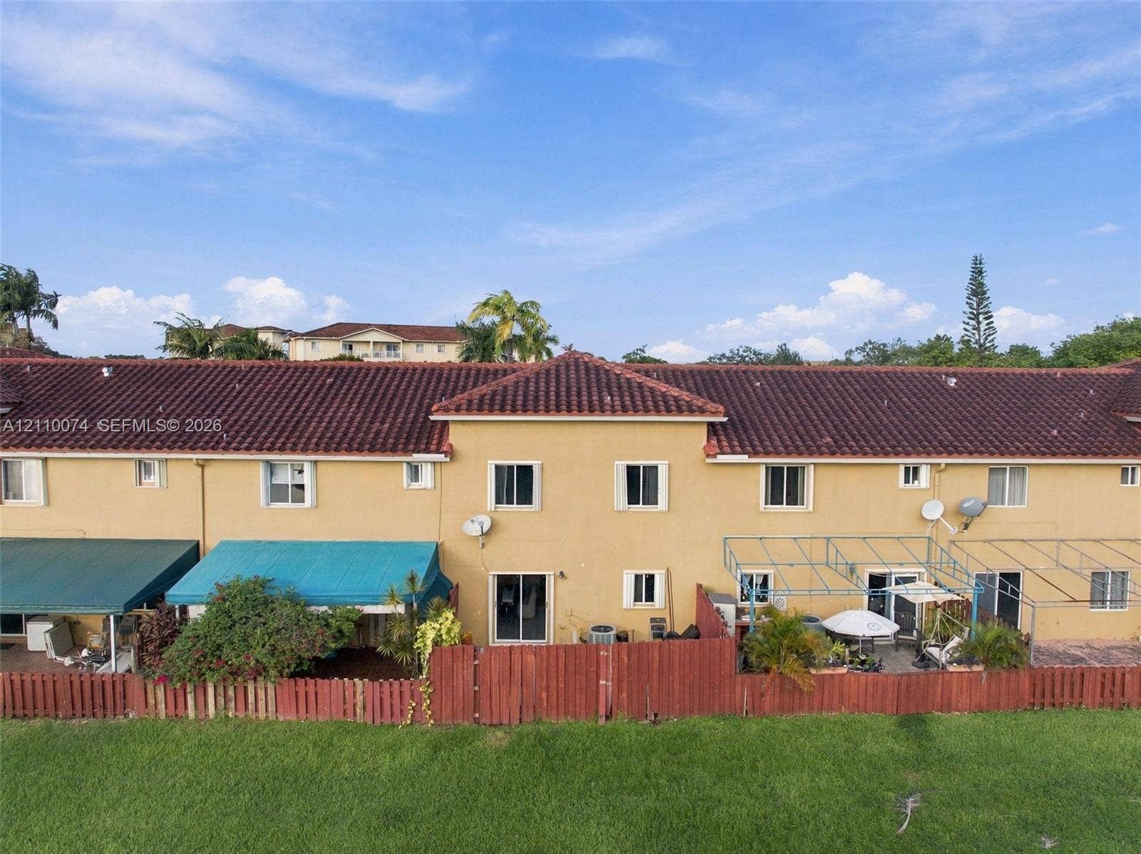 17370 NW 69th Court, #304, Hialeah, FL 33015 Exterior elevation featuring a stucco facade, red tile roofing, rear patio enclosures, and wood-style privacy fencing overlooking a grassy lawn