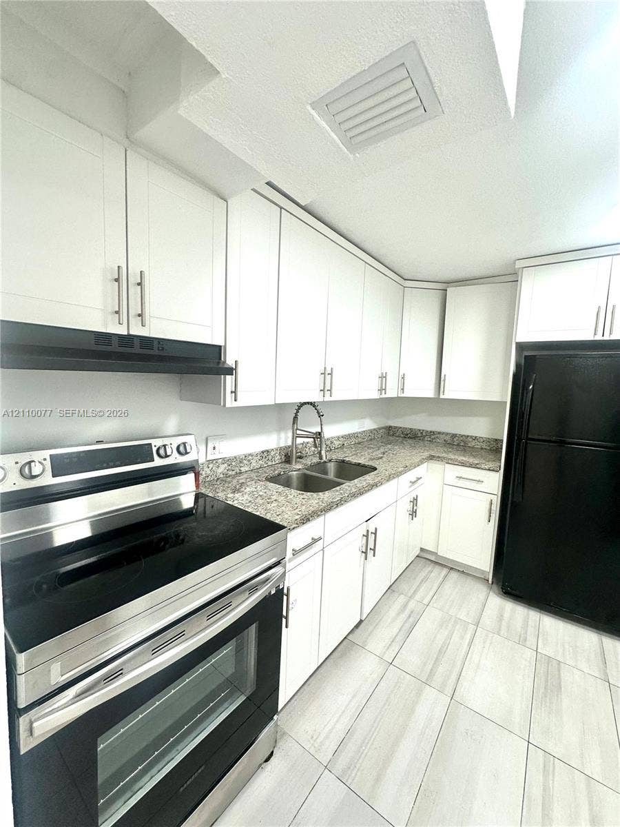 Kitchen featuring white shaker-style cabinetry, stone-finish countertops, dual-basin stainless steel sink with pull-down faucet, black kitchen appliances, and light-toned tile flooring