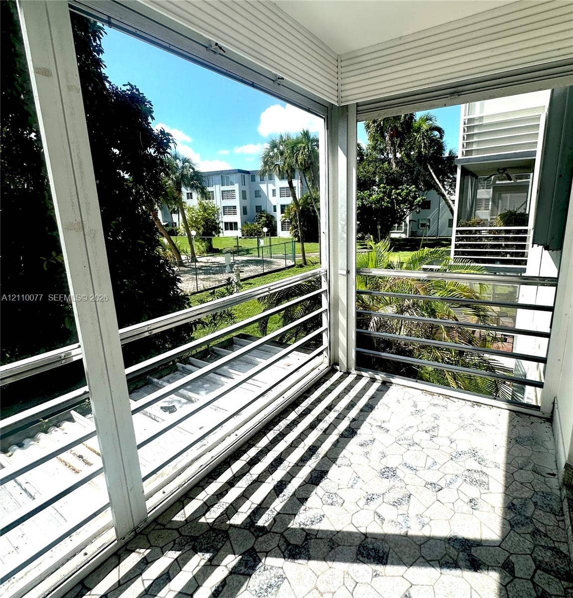 Enclosed balcony featuring a horizontal metal railing system, geometric stone-patterned tile flooring, and white paneled ceiling