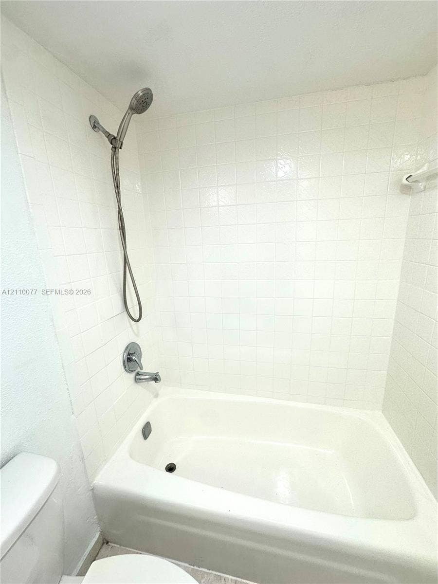 Full-height white square tile surround, tub-shower combination with a handheld shower fixture, and polished metal plumbing hardware