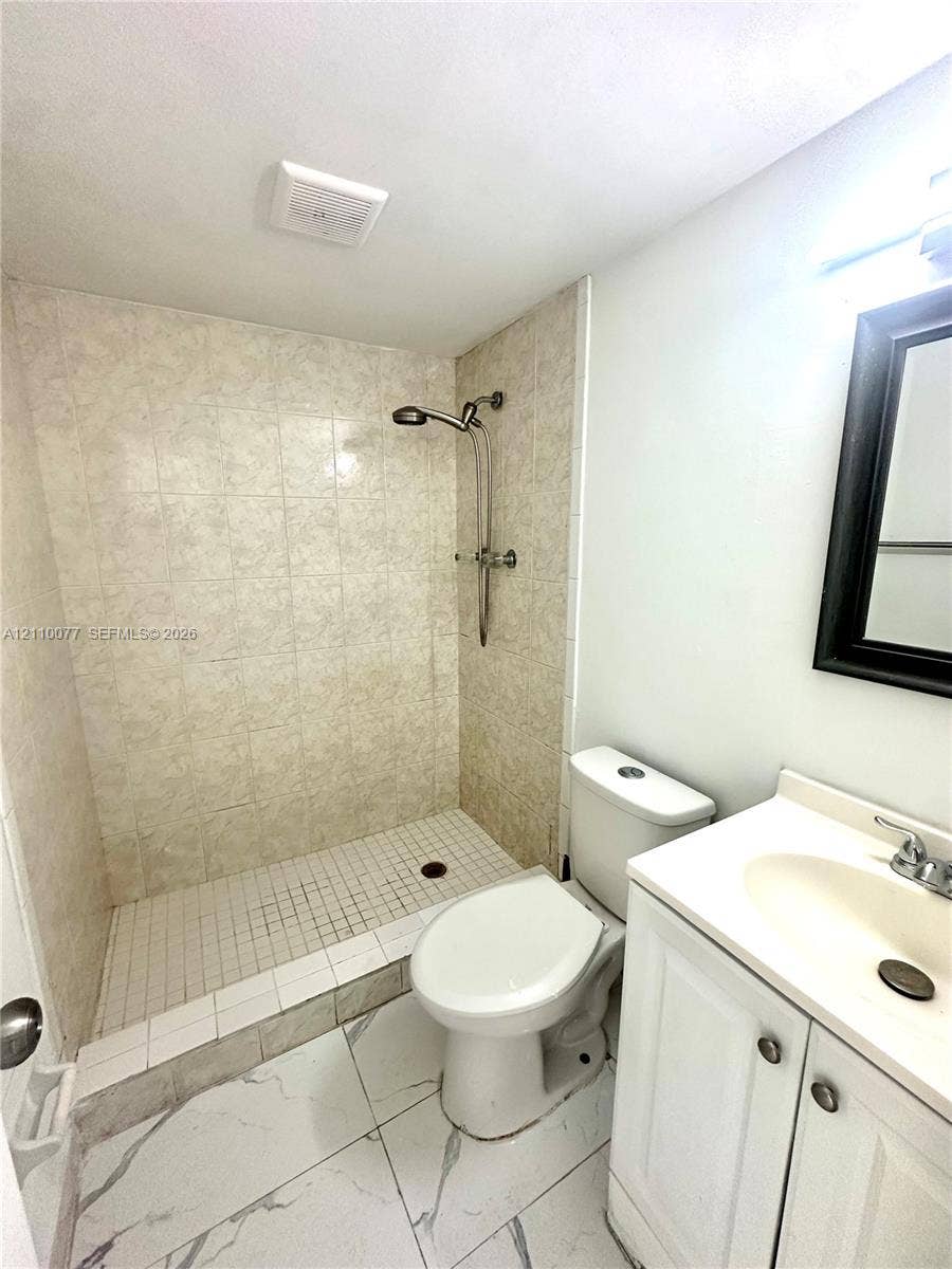Walk-in shower with stone-patterned wall tile, white vanity featuring a molded sink, and large-format tile flooring with marble-style veining