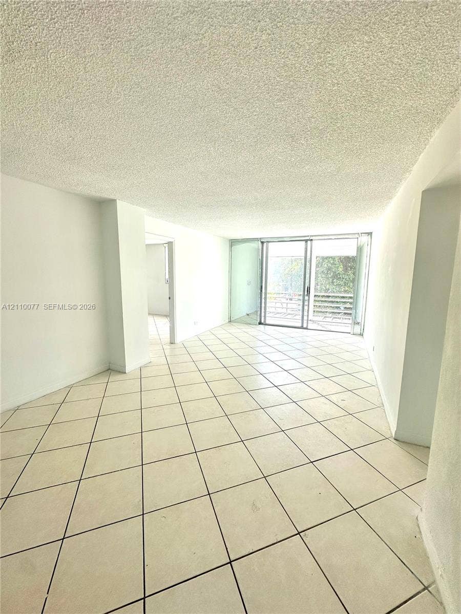 Interior space featuring white-toned ceramic tile flooring, textured ceiling finish, and glass sliding doors providing exterior access