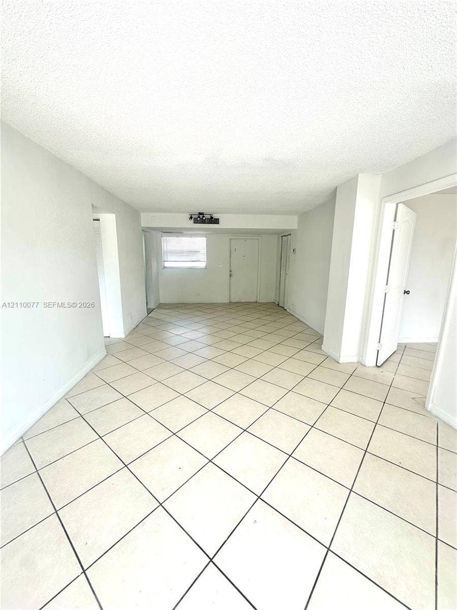 Neutral interior space featuring large-format diagonal tile flooring, textured ceilings, and an exterior entry door with a rectangular window