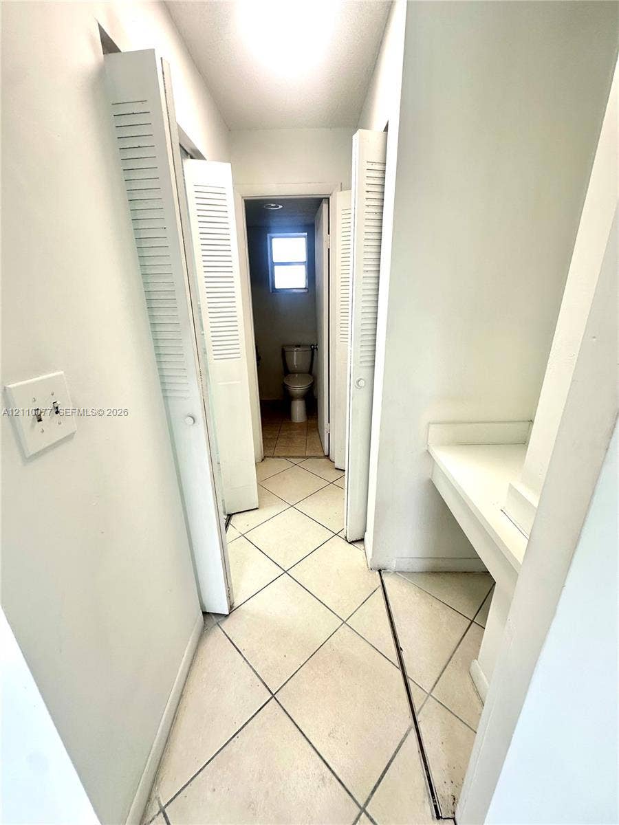Hallway featuring diamond-patterned tile flooring, louvered closet doors, and built-in counter space