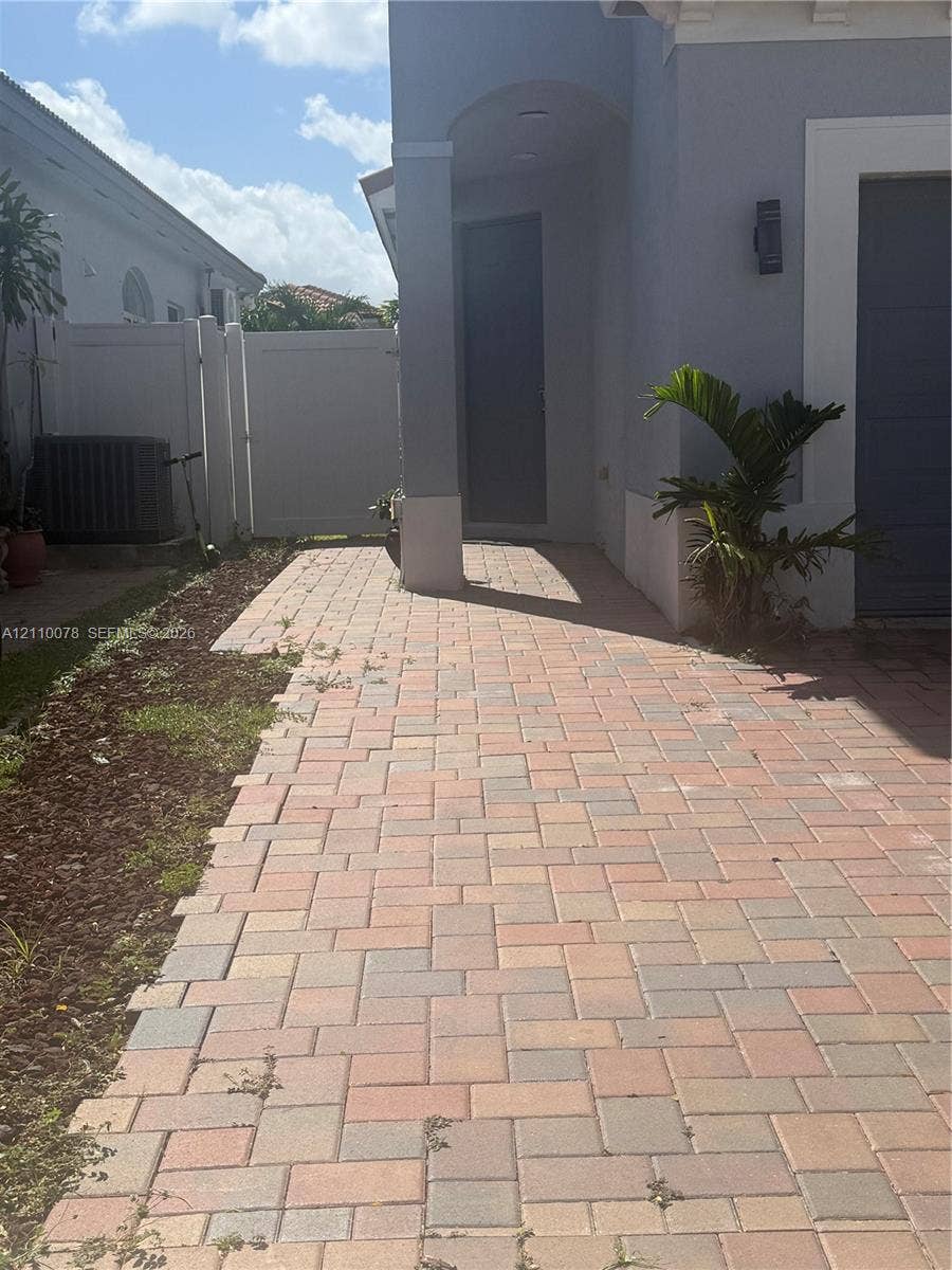 Concrete paver side walkway featuring a covered entryway with a recessed ceiling and a solid-panel door