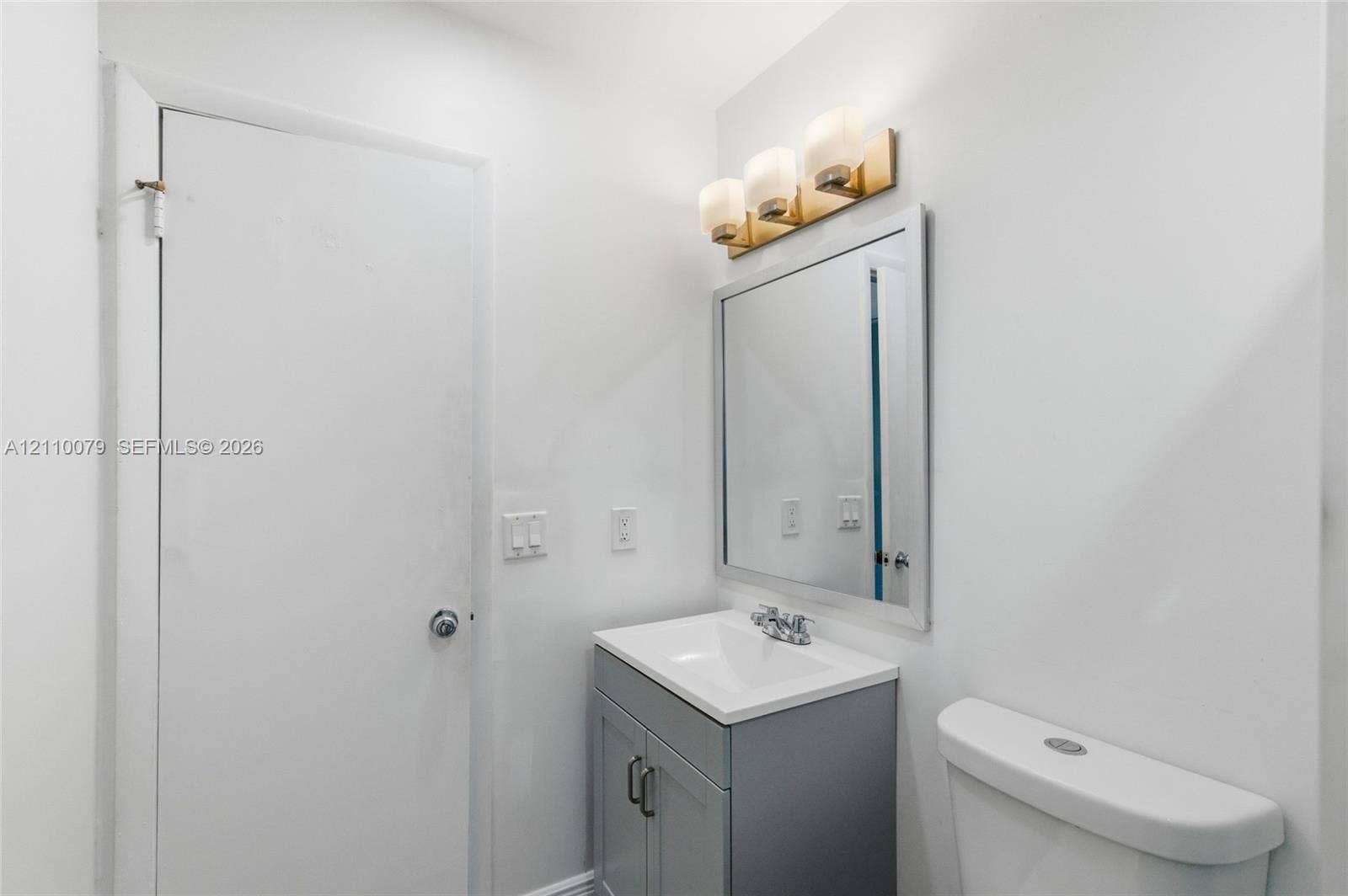 4106 NW 88th Avenue, #3, Coral Springs, FL 33065 Gray vanity with a white countertop and basin, three-light fixture with glass shades, and a rectangular mirror with a metal frame