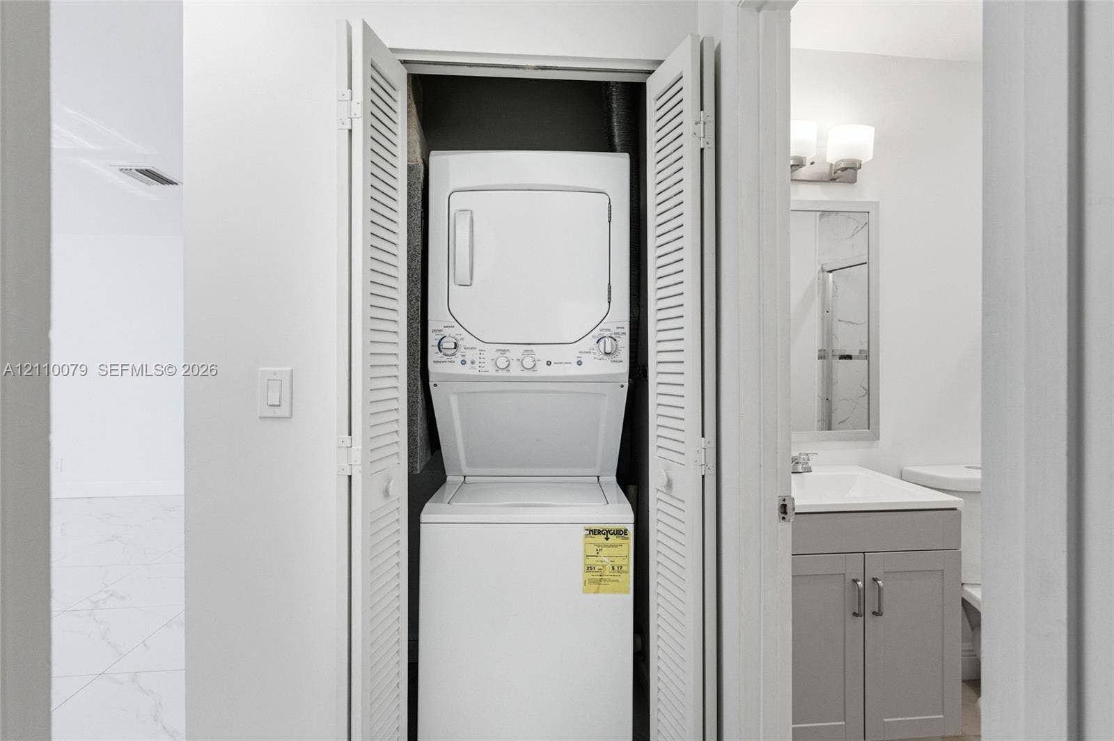 4106 NW 88th Avenue, #3, Coral Springs, FL 33065 Laundry closet featuring louvered bi-fold doors, white stacked laundry unit, grey vanity cabinet with solid surface countertop, and wall-mounted vanity lighting
