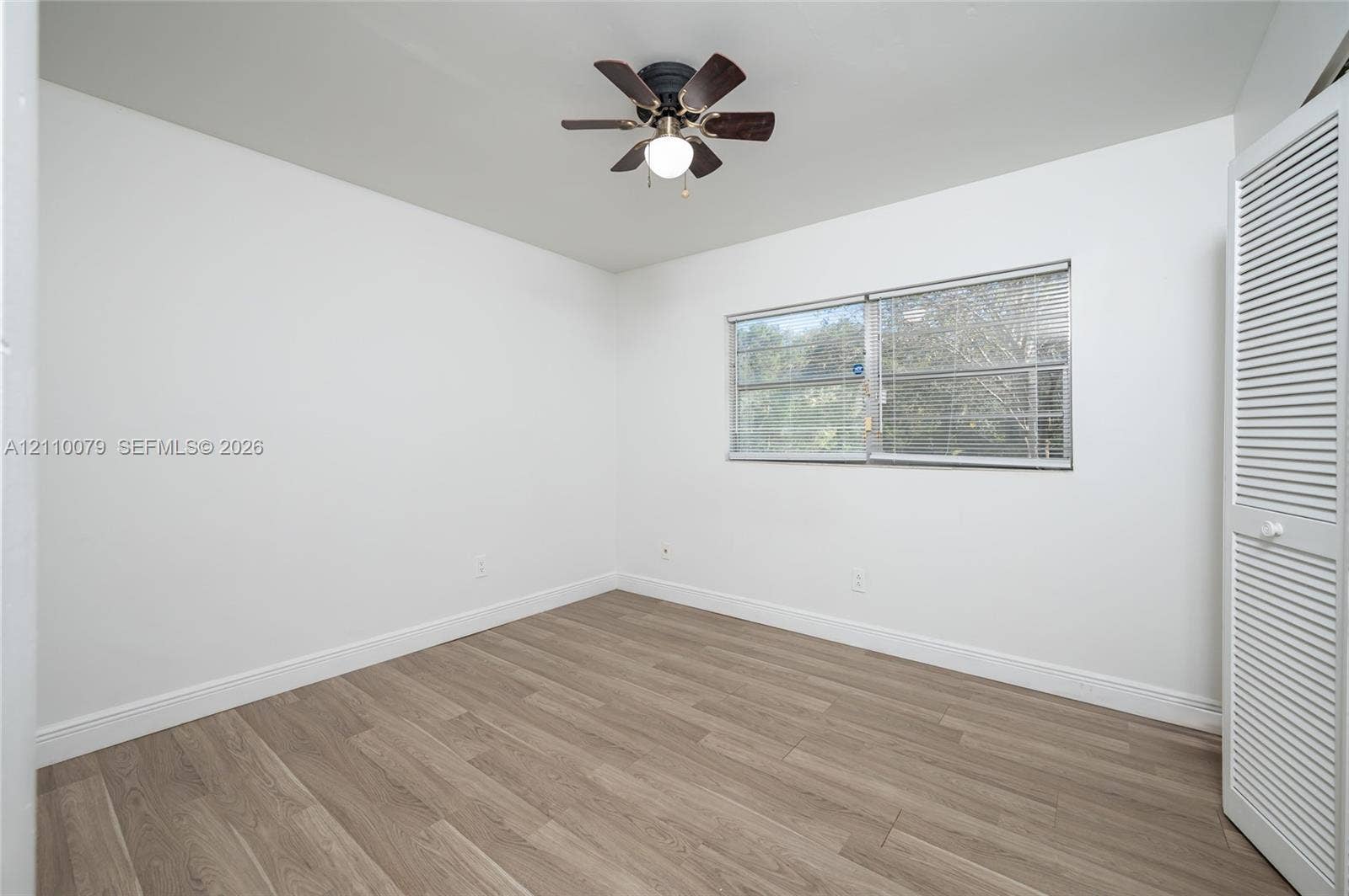 4106 NW 88th Avenue, #3, Coral Springs, FL 33065 Neutral-toned wood-finish flooring, white walls, louvered bi-fold closet doors, and a ceiling fan with integrated lighting