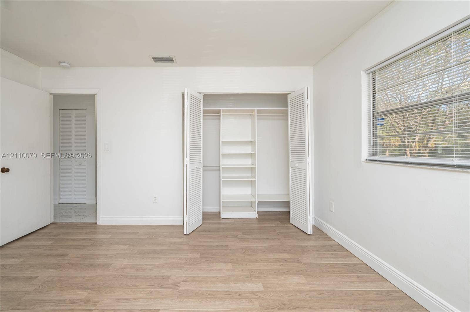 4106 NW 88th Avenue, #3, Coral Springs, FL 33065 Room interior featuring wood-finish flooring, a window with horizontal blinds, and a closet with bifold doors and built-in shelving