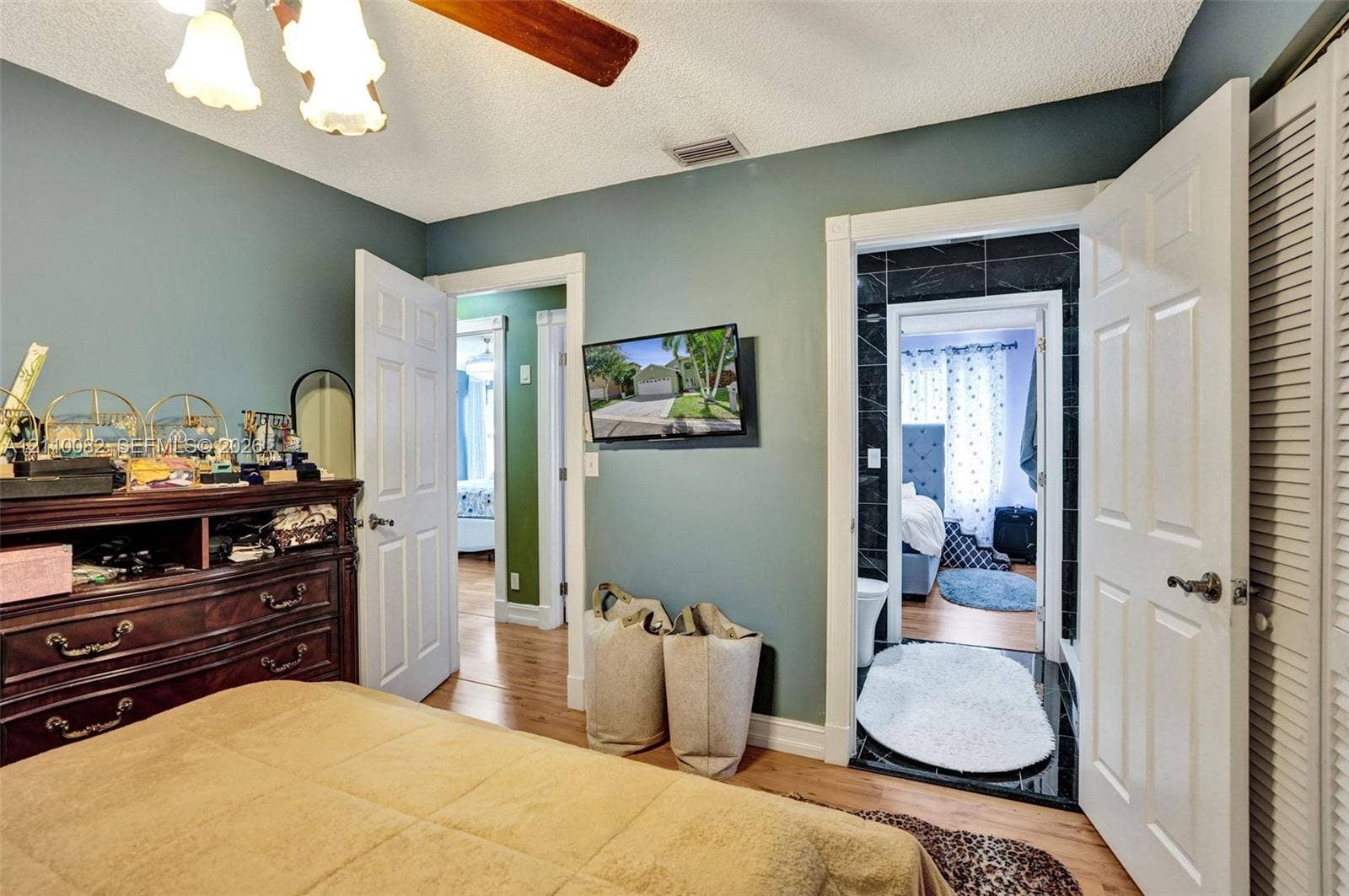 Bedroom featuring wood-finish flooring, ceiling fan with light fixture, louvered closet doors, and interior access to a bathroom with tile surround