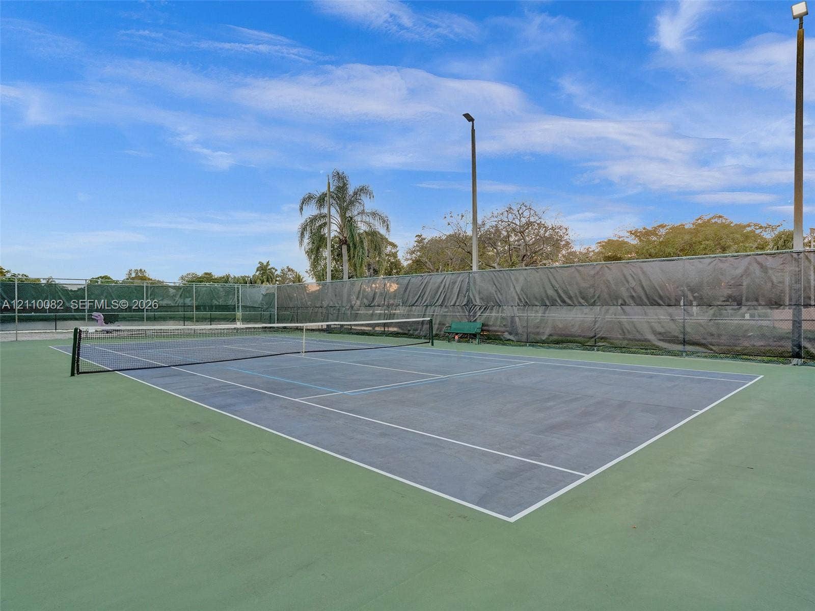 Tennis court featuring a paved playing surface, perimeter chain-link fencing, privacy screens, and integrated lighting poles