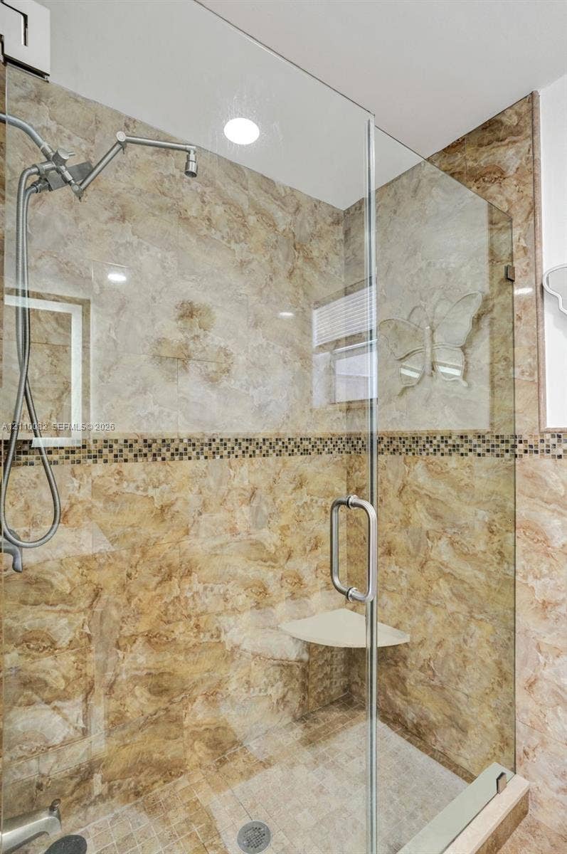 Walk-in shower featuring glass enclosure, stone-finish wall tile, decorative mosaic tile inlay, built-in corner seat, and adjustable showerhead