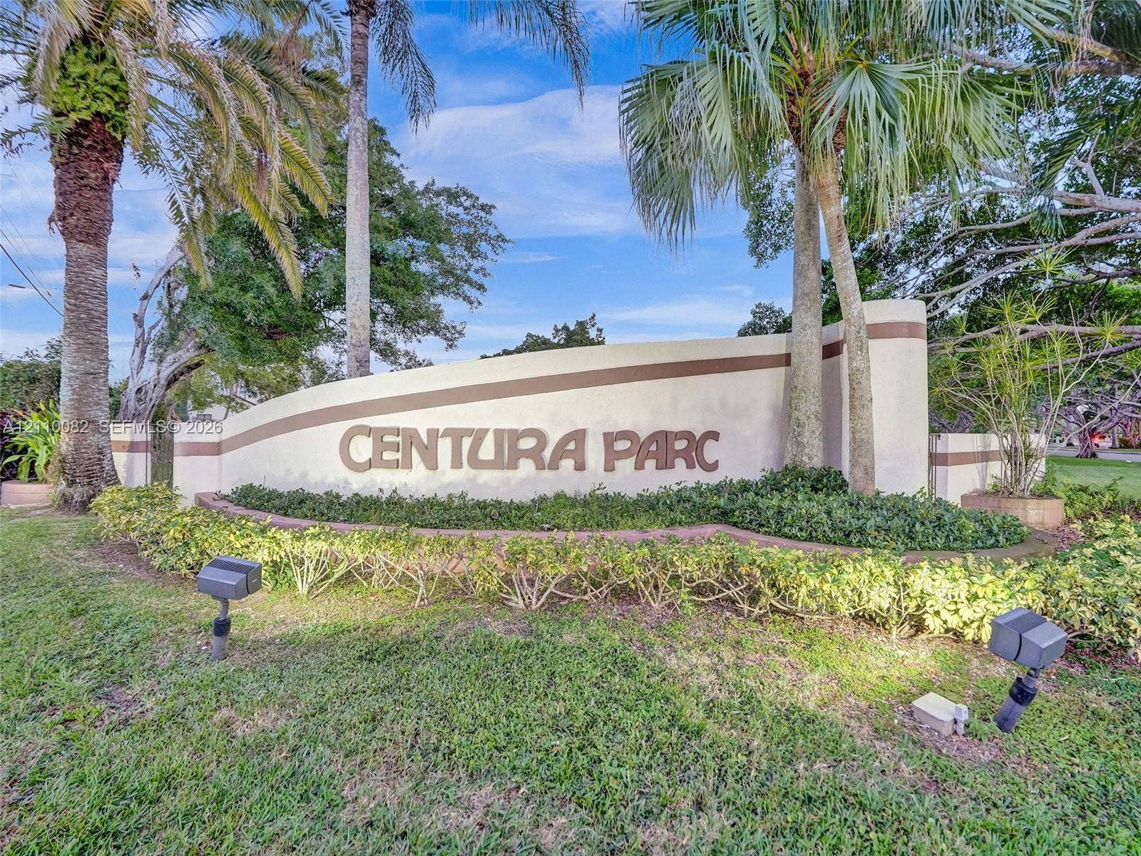 Monolithic stone-finish entrance monument featuring dimensional lettering, decorative accent bands, manicured low-profile hedges, and mature palm trees