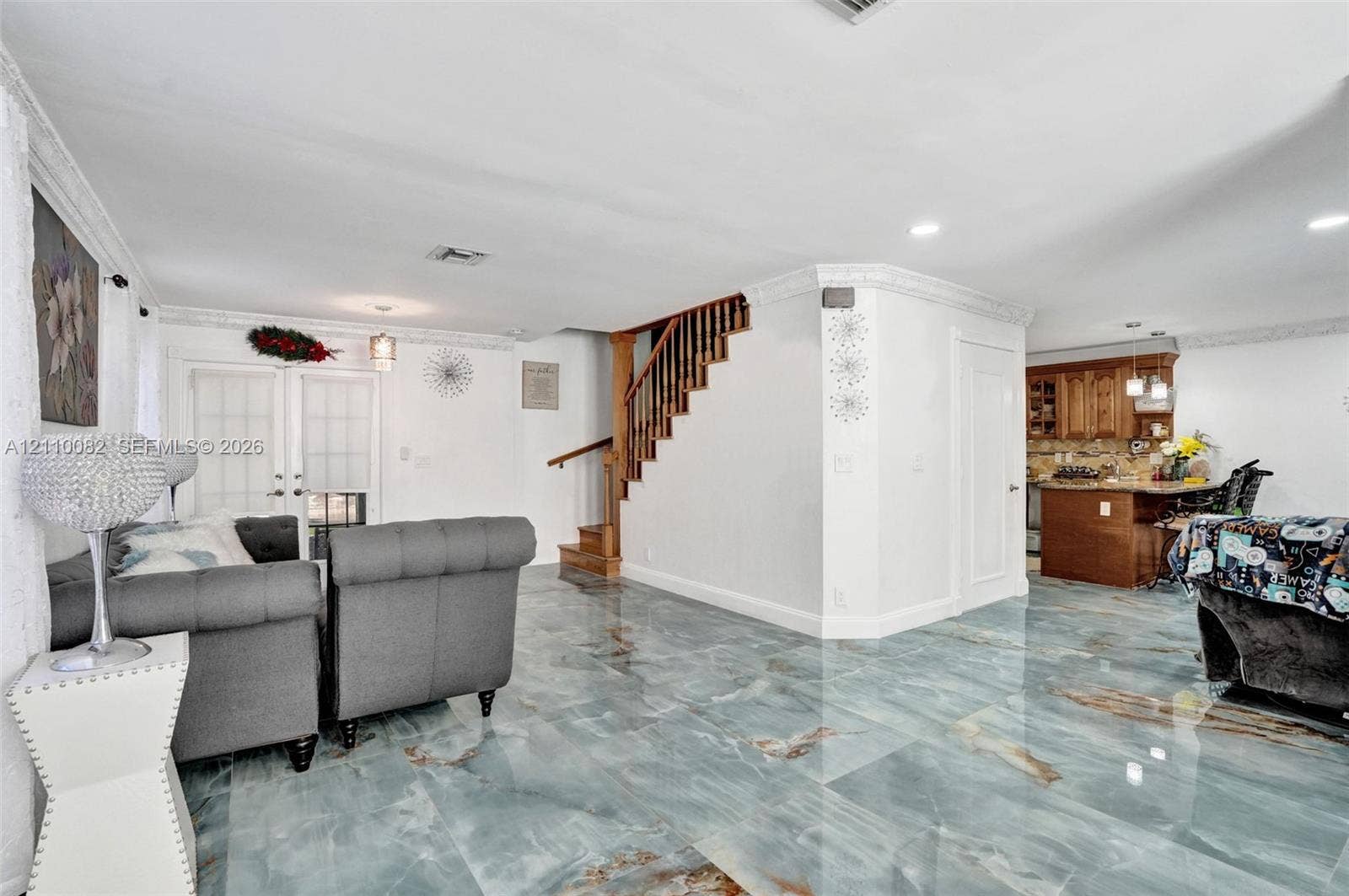 Large-format polished stone flooring with distinct veining, crown molding, wooden staircase with slatted balustrades, and recessed ceiling lighting
