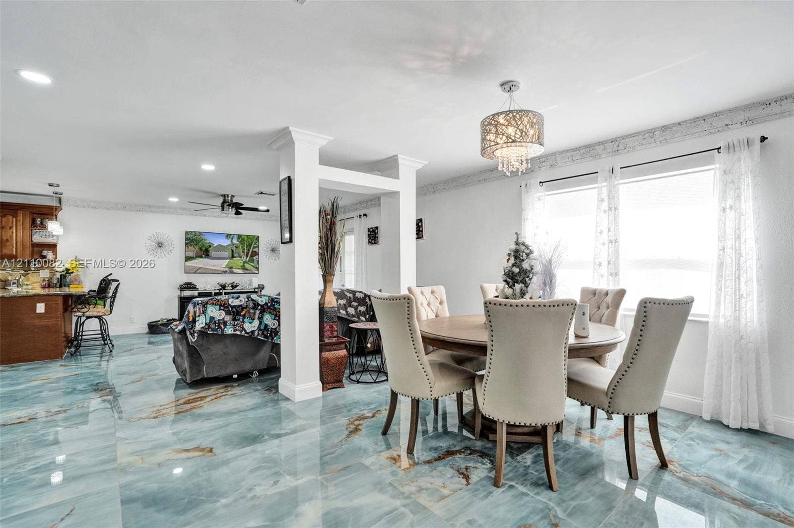 Large-format polished tile flooring, recessed ceiling lighting, decorative tiered crystal chandelier, and custom structural columns