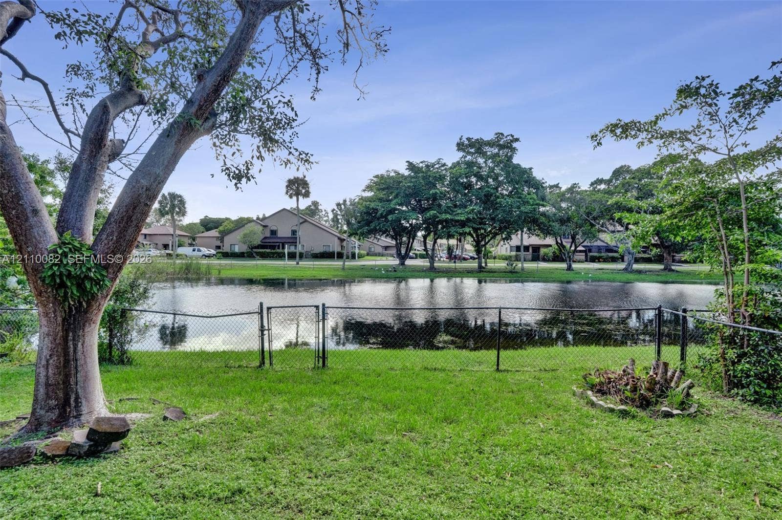 Backyard featuring a grass lawn, chain-link perimeter fencing, mature trees, and a water frontage